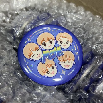 A blue circular button or badge features chibi-style cartoon characters and a rainbow cat design, sitting on bubble wrap.