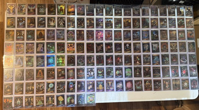 A large collection of the "Fuzzy Cards" NFT set (cards 1-150), tied to the $FUZZY token on the XRP (XRP Ledger) blockchain, is displayed in protective sleeves laid out on a table. The cards feature colorful fantasy artwork and are being shown to estimate the set's total value.