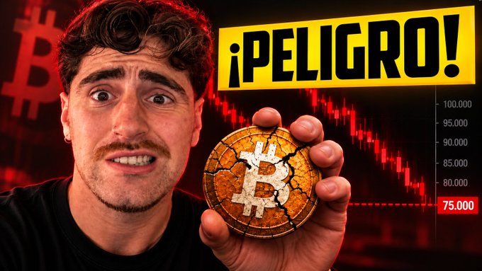 A man with a shocked expression holds a cracked Bitcoin coin against a background showing a red Bitcoin price chart, with a yellow banner reading '¡PELIGRO!' and prices ranging from 75,000 to 100,000.