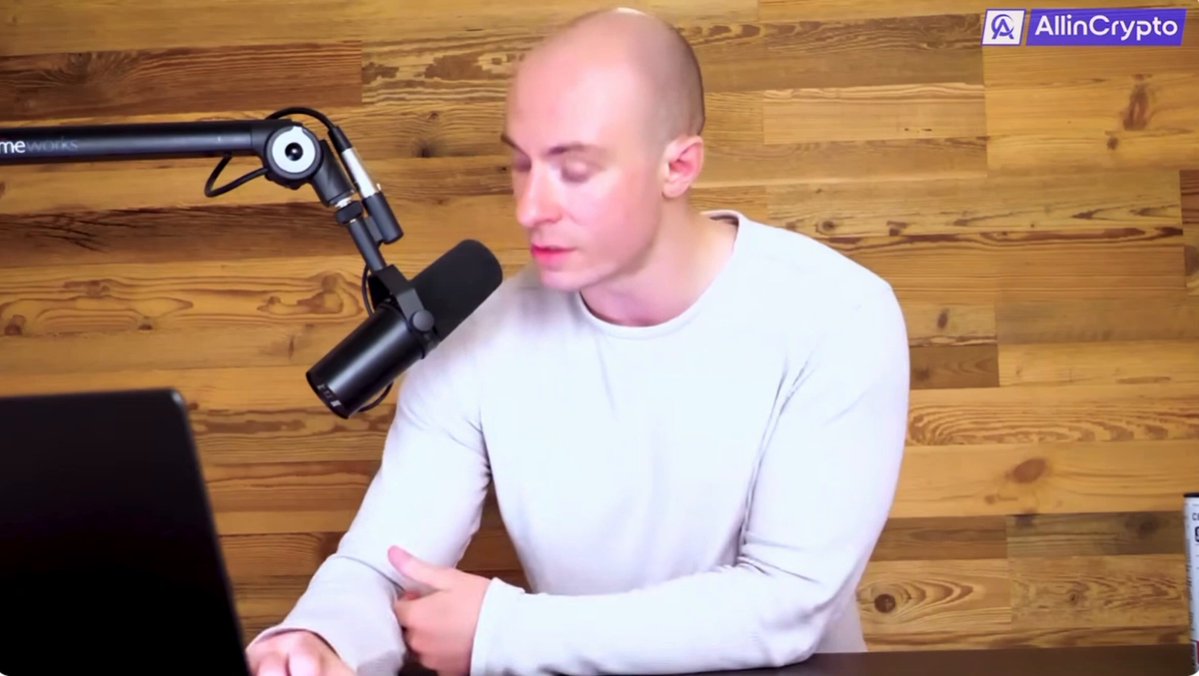 The image features a bald man wearing a white shirt sitting at a desk with a laptop computer, giving off an impression of him working or engaging in some sort of online activity. The background consists of wooden walls, which could be part of a home office setup. There is also a microphone present on the desk, suggesting that he might be involved in podcasting or other audio-related activities. The caption "XRP the future!" implies that the man may be discussing or promoting cryptocurrency, possibly related to his work or personal interests.