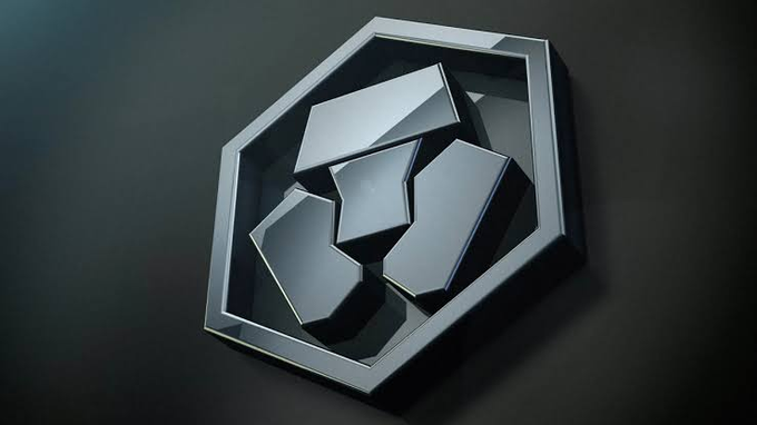 A 3D-rendered metallic hexagonal emblem features fragmented geometric shapes inside a polished frame against a dark background.