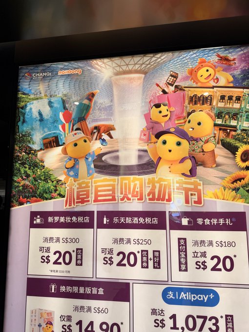 A colorful advertisement for Changi Airport at Jewel promotes a shopping festival featuring cartoon mascot characters, with promotional offers in Chinese including '樟宜购物节' and discounts via Alipay.