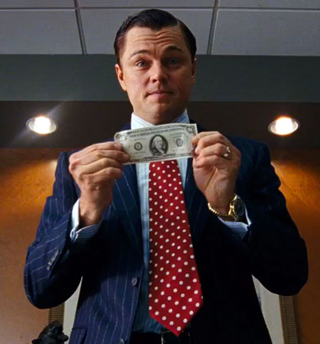 A man in a pinstripe suit with a red polka-dot tie holds up a one-dollar bill with both hands, showing a smug, satisfied expression. The image humorously responds to the recruiter's question by suggesting that money—specifically a single dollar—is the sole motivation.