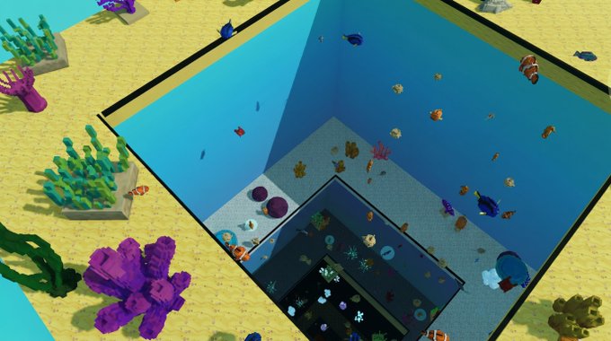A top-down view of an underwater aquarium exhibit featuring colorful fish, coral, and plants in blue water beside a sandy area with green and purple plants.