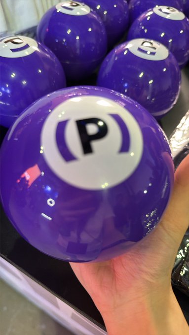 A close-up of purple lottery balls with the letter 'P' printed on them, with one ball held in a person's hand in the foreground.