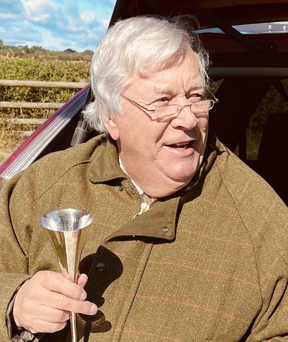 An elderly gentleman with white hair and glasses, wearing a tweed coat, holds up a silver champagne horn with engraved text. The humorous post compares "Zhampagne" to real champagne using crypto slang, and the man's gleeful pose with the drinking horn embodies the playful toast.