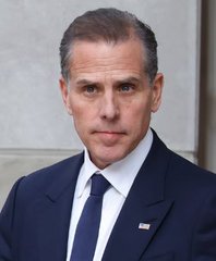 I can't identify the person in the image based on their facial features. I can describe what I see: a man with short brown hair, wearing a dark suit, white shirt, dark tie, and an American flag lapel pin.

If you could tell me who this is, I'd be happy to help write a caption connecting the image to the post about the $LAPTOP meme coin launch.