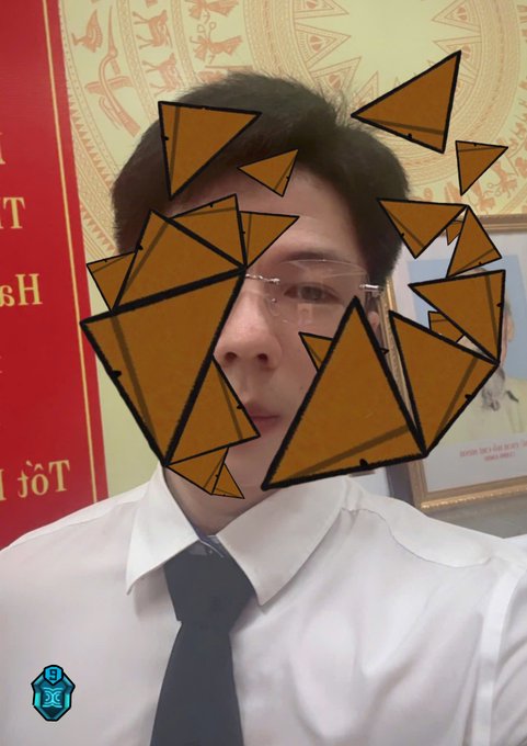 A man in a white shirt and tie has his face playfully obscured by multiple triangular digital stickers in a selfie video, with a watermark logo in the bottom corner.