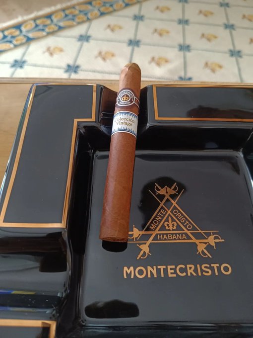 A Montecristo cigar labeled "Colección Vintage" rests on a black Montecristo Habana ashtray with gold trim and fleur-de-lis emblems.