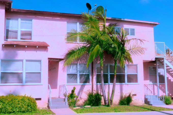 The image features a pink building with two palm trees growing outside of it, situated on a street corner. The photo appears to be taken from across the street, providing a clear view of the building's exterior. There are no people visible in the image, which adds to its serene atmosphere. The post accompanying this image is titled "Thank you so much to the guys who collected from The Photo Collection this weekend! what a nice thing to see on a Monday morning California Dreamin x xtz and Familiars @fangsfilms 5 left at 11:11". This message seems to be related to the pink building, as it is described as "a beautiful pink building with two palm trees growing outside of it" and "the photo was taken from across the street".