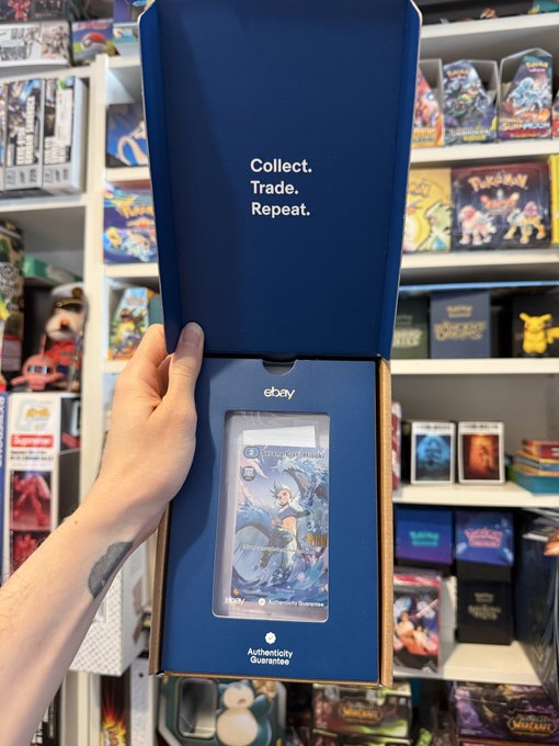 A hand holding an opened eBay Collect, Trade, Repeat blue box containing a graded anime trading card, with shelves of Pokémon card products visible in the background.
