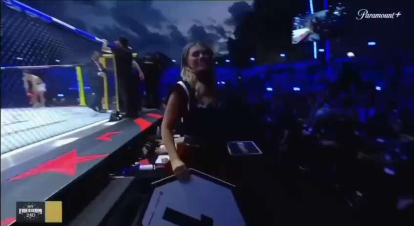 The image shows a woman standing behind a table with a sign that says "most stablecoins never leave crypto $USD1 went from staking products and liquidity pools to paying performance bonuses at a UFC event hosted at the White House." The woman is smiling, possibly indicating her excitement about the event or the coins she has been holding. The image also includes text that reads "most stablecoins never leave crypto $USD1 went from staking products and liquidity pools to paying performance bonuses at a UFC event hosted at the White House," which seems to be related to the content of the post.
