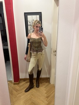 A woman takes a mirror selfie wearing a corset-style top, cream-colored leggings, brown knee-high boots, and a leopard print headscarf, with the post referencing "Odetta." The mirror reflection reveals an art print on the wall behind her, complementing the curated, vintage-inspired outfit.