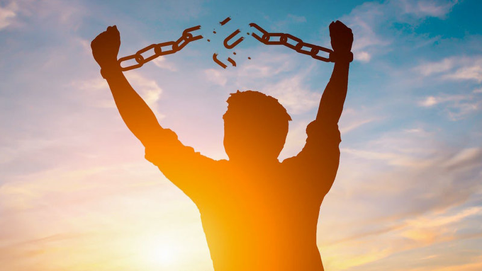 A silhouette of a person breaking free from chains with raised arms against a sunset sky, symbolizing liberation and freedom.