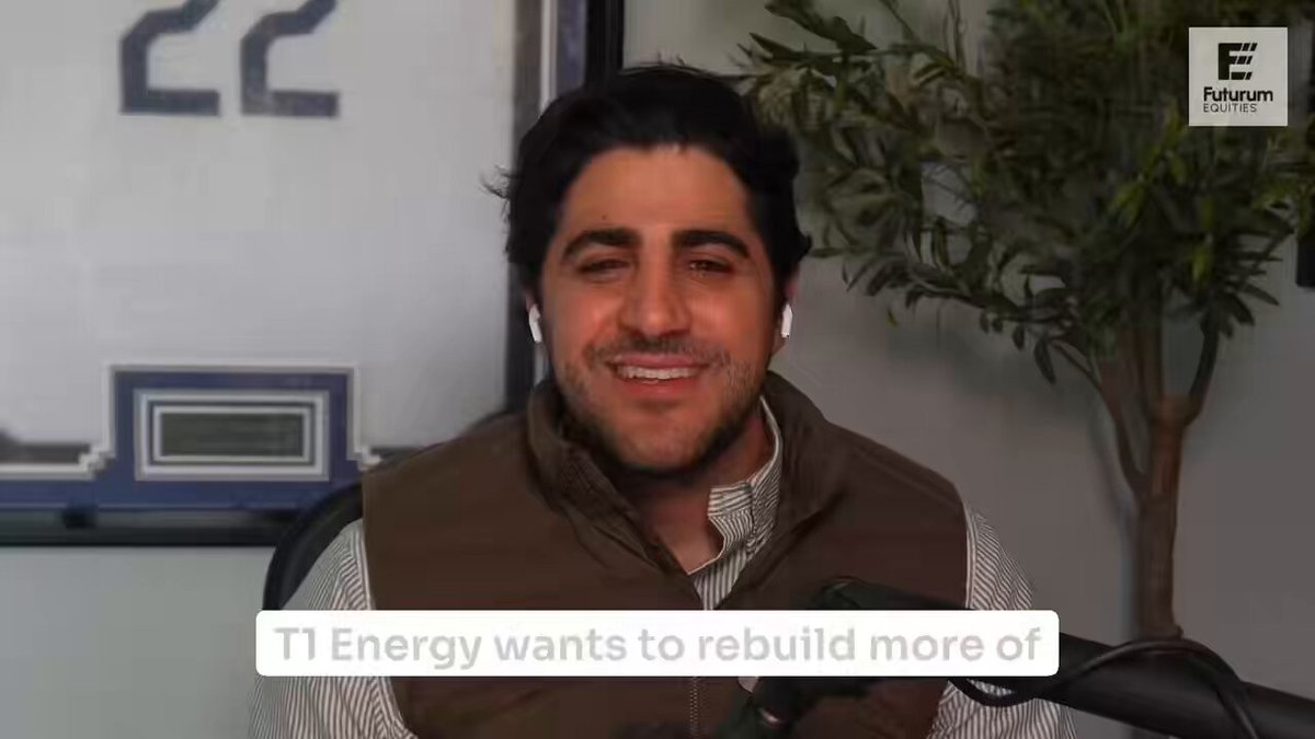 A man wearing a brown vest and with headphones sitting at a desk, smiling for the camera while speaking into a microphone. The backdrop features an electrical outlet. The image appears to be part of a media campaign or article related to clean energy infrastructure development in the United States.