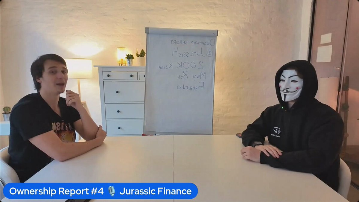 The image shows two people sitting at a table with their hands crossed over each other's shoulders. One person has a mask covering their face while the other person wears a hoodie. The background features a white wall, a desk with a lamp on top of it, and a whiteboard hanging on the wall. There is also a plant in the room. The post reads "Solana, uh, finds a way."