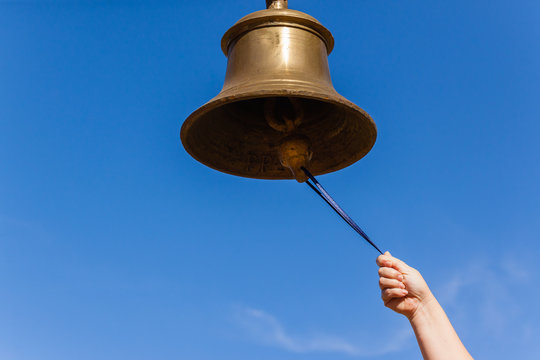 A hand reaches up with a stick to ring a large brass bell against a clear blue sky, symbolizing a "call to action" or an exciting announcement—fitting the celebratory tone of "Let's go.." paired with the #XRP hashtag, likely marking a bullish moment for the Ripple cryptocurrency.