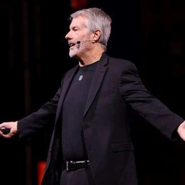 A man with gray hair and beard speaks passionately into a headset microphone while gesturing with his arms extended on a dimly lit stage. His dynamic presentation style reflects the bold claims in the accompanying post, which highlights Michael Saylor's announcement that Strategy's Total Reserve Capital now exceeds every S&P 500 financial services company except Berkshire Hathaway.