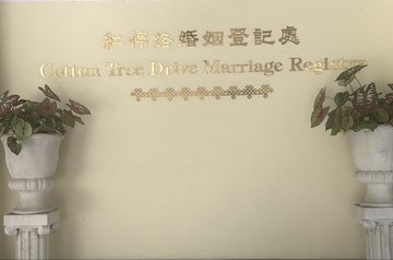 A reception sign for 'Cotton Tree Drive Marriage Registry' with Chinese characters above, set between two white decorative pedestals holding flower arrangements.