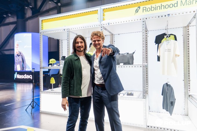 Two men pose together at the Robinhood Market HOOD Summit, with one pointing toward the camera beside a display booth showcasing branded apparel and a Nasdaq sign visible in the background. The image captures the post's announced conversation about Robinhood's tokenization plans and Chain roadmap, taken right on the summit floor moments after the interview.