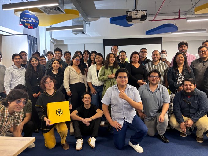 A large group photo of around thirty people posing together in a modern office space, with a blue balloon reading 'Somos Top Employer 2026' floating above.