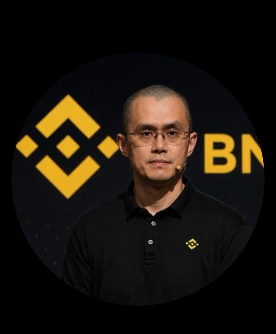 A man wearing glasses and a black polo shirt with the Binance logo, standing in front of a backdrop featuring the Binance logo and symbol.