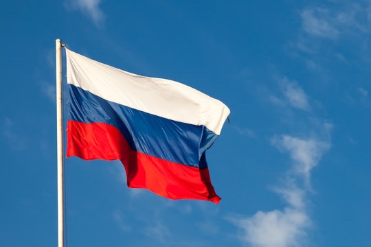 The Russian flag waves against a blue sky, visually representing the country behind Sberbank's recent approval to launch crypto custody services and digital asset products, including Bitcoin, Ethereum, and USDT. The image underscores the national significance of Russia's largest bank entering the cryptocurrency industry.