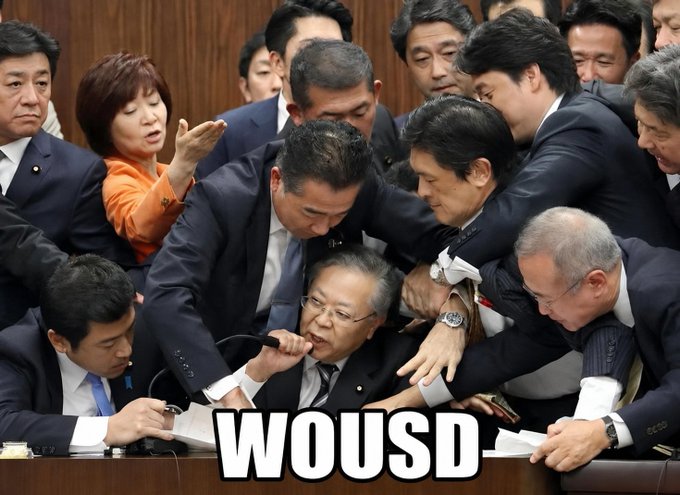A chaotic political scene shows several Asian officials in suits crowded together, with an elderly man at the center appearing to be restrained or assisted by others as he grabs a microphone. The text "WOUSD" is overlaid at the bottom in large bold letters. The image's depiction of a frantic, grasping crowd humorously illustrates the post's promise of high-yield APYs, suggesting a frenzy of investors trying to seize the lucrative 618% Long and 17% LP returns.