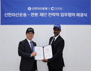 The image shows two men dressed in suits holding a document together, possibly a contract or agreement. The text of the document suggests that they have signed an agreement with Canton Foundation, which could be related to their business interests. The background features a banner displaying the Canton Foundation's name and logo, indicating that this event is taking place at a Canton-based venue.