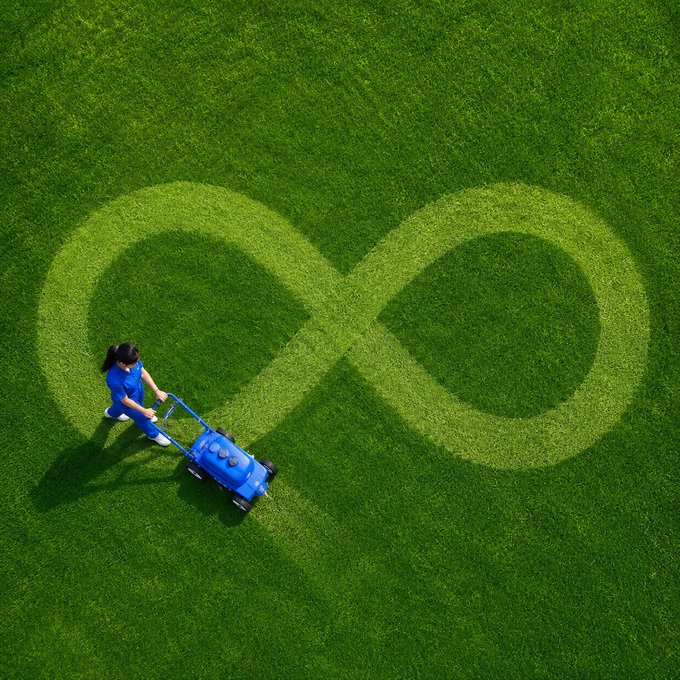 An aerial view of a person pushing a lawnmower across green grass, leaving an infinity symbol pattern cut into the lawn.