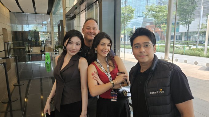 A group of four people pose together for a photo in a modern lobby, with one man wearing a vest labeled 'Kotani Pay'.