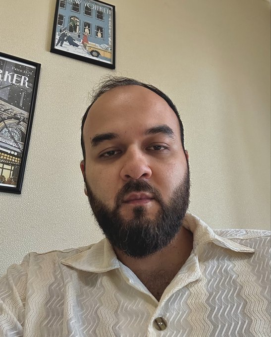 The image features an adult male with a beard wearing a white shirt, sitting down with his face towards the camera. He has a slight smile and appears to be enjoying himself as he takes a selfie for someone else to see. The photo includes text that reads "Day 45 of posting selfie until $chog hits 1$ Price 0.0018M Despite my birthday, there should be a selfie today." This suggests that this man is actively engaging in the act of taking a selfie on a certain day and documenting his activities with the post's accompanying message.