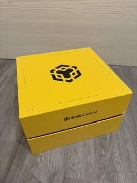 The image features a yellow box with black text that reads "BNB Chain" written on it, placed on a wooden floor. The box has two sides, one of which is open, revealing its contents inside.