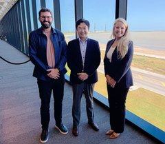 Three people (two men in suits and one woman in a black blazer) posing together for a photo at what appears to be a racetrack venue.