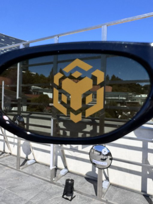 A large BNB Chain logo is displayed on the lens of an oversized sunglasses sculpture at an outdoor pop-up installation, with a coin labeled "BNB Chain" visible below, reflecting the "Build BNB Chain Seoul pop-up" event.