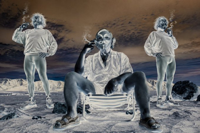A surreal, vintage-style photograph featuring three figures with painted faces in a desolate landscape, with the central seated figure smoking a cigarette on a beach chair.