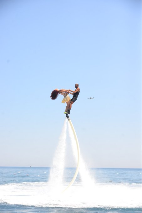 Two people perform an impressive flyboard stunt high above the ocean, with the woman being lifted and spun by the man as powerful water jets propel them into the bright blue sky. The exhilarating airborne moment captures the carefree, soaring feeling the post describes, perfectly matching the excitement of crypto gains and an amazing holiday in Turkey.