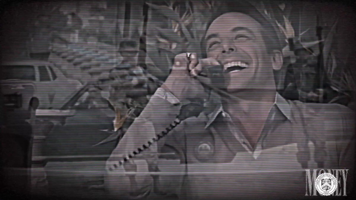 The image shows a man talking on his cell phone with a smile, wearing a shirt that says "Grade A content coming from $MONEY Should cook nicely for us imo, narrative is like $JOB, $RETIRE, $NOTHING". The background of the image features a car and trees.