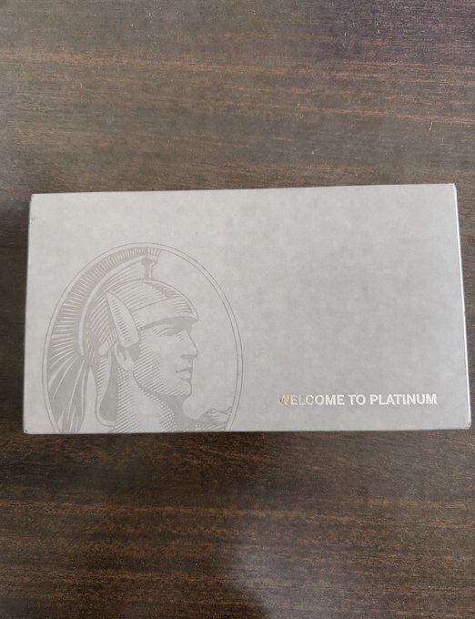 A silver "WELCOME TO PLATINUM" card featuring an embossed profile of a figure in a helmet, resting on a dark wooden surface.