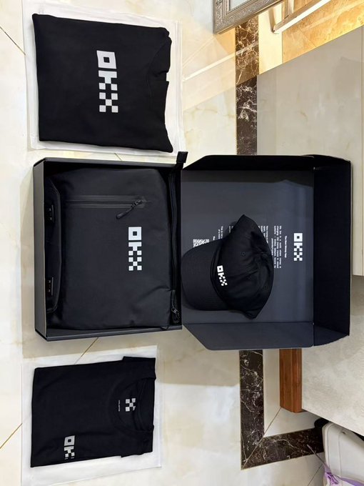 Black clothing items including t-shirts and a backpack are displayed in branded packaging with a pixelated checkered logo.