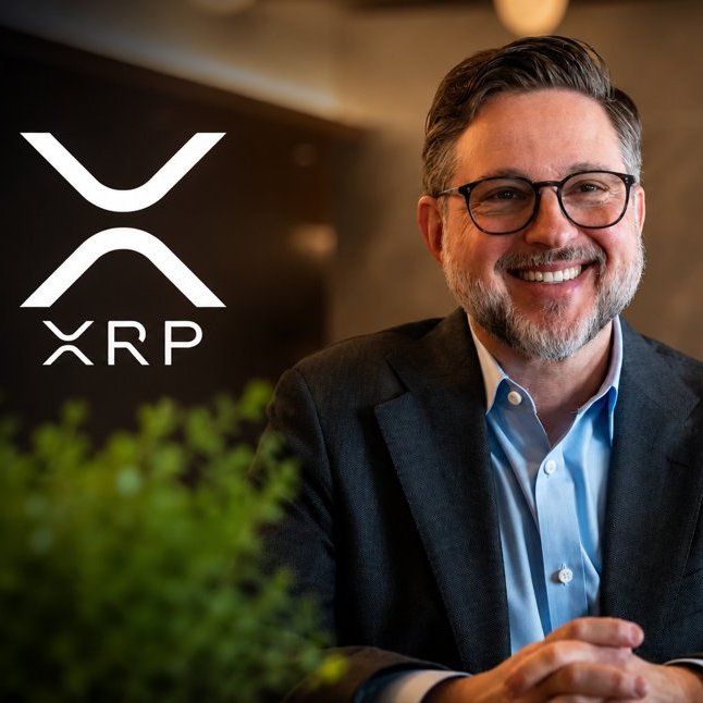 A smiling man with glasses and a beard in a dark blazer and light blue shirt, positioned next to the white 'XRP' cryptocurrency logo on a dark background.