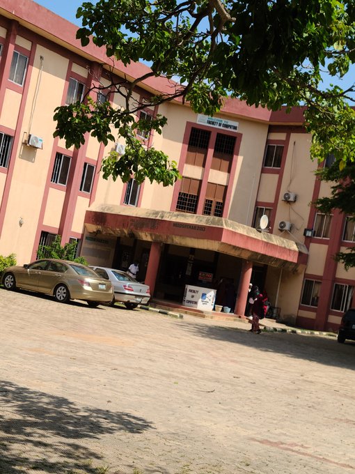 A photograph of a multi-story pink and tan building labeled 'FACULTY OF EDUCATION' with cars parked in front and a tree branch framing the top of the image.