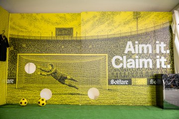 A large yellow banner featuring a soccer goalkeeper mid-save advertises Solflare with the slogans "Aim it. Claim it." and "Soflare," accompanied by soccer balls at a .debug conference booth in Croatia, tying into the company's promotion of FIFA World Cup 2026 fan engagement.