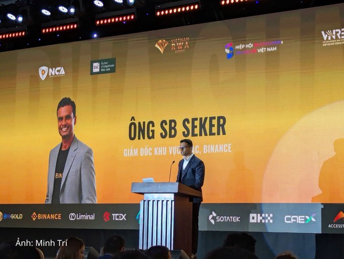 A man speaks at a podium during the 'Vietnam RWA' conference; the screen behind him displays 'ÔNG SB SEKER, GIÁM ĐỐC KHU VỰC, BINANCE' alongside logos for sponsors including Binance and OKX.