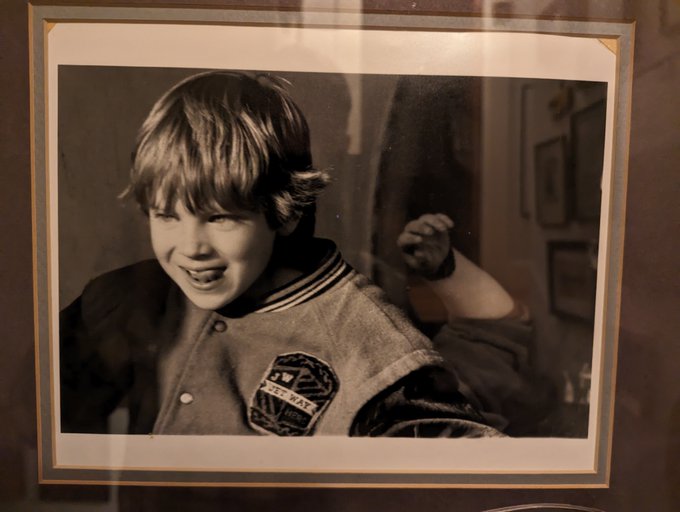Black and white framed photograph of a young boy in a 'Blue Wave' jacket smiling.
