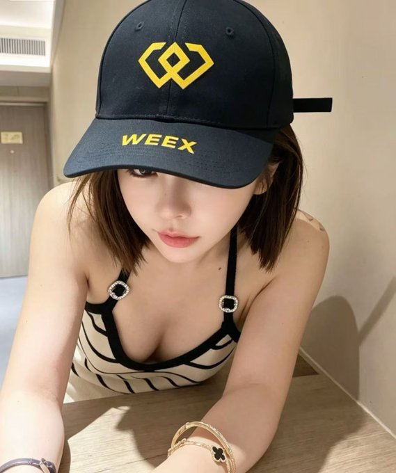 A selfie of a young woman wearing a navy blue WEEEX branded cap and a black-and-white striped top, showing a tattoo on her shoulder.