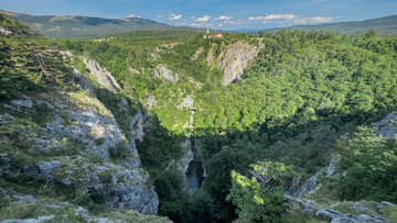 A dramatic aerial view of a deep, forested canyon with a tall waterfall cascading down its rocky cliffs, contrasting with the post's promotion of limited-edition "NEVERMIND" (33 editions) and "Apéritif" (4 editions) pieces from the #THESNAILEVENT collection. The vast natural landscape serves as a serene backdrop that mirrors the exclusive, almost hidden nature of these small-run collectibles.