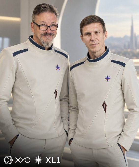 Two men wearing matching futuristic white uniforms with blue and purple accents, posing together with 'XO' and 'XL1' logos at the bottom.