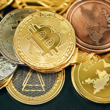 A close-up of physical cryptocurrency tokens, prominently featuring a gold Bitcoin coin with its iconic "₿" symbol at the center, surrounded by other gold and silver crypto coins, visually representing the growing adoption of crypto-based payments referenced in the report.