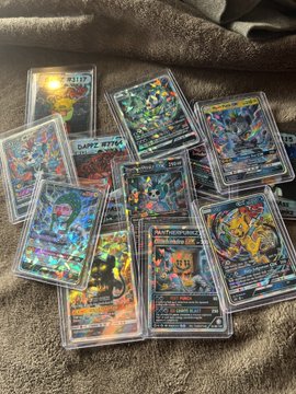 A collection of holographic Pokémon trading cards is scattered on a gray fabric surface, with names like 'Keldeo', 'Darkrai', and 'Tornadus' visible.